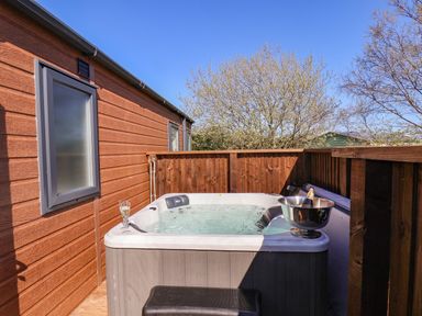 An outdoor hot tub with a glass of drink and a bottle in an ice bucket on a wooden deck at Honeysuckle Lodge in Runswick Bay near Staithes
