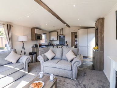 A living room with two grey sofas a wooden coffee table with pastries and cups and an open kitchen area at Honeysuckle Lodge in Runswick Bay near Staithes