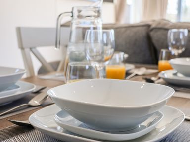 A dining table set with white plates, bowls, glasses, cutlery, a jug of water, and glasses of orange juice at Honeysuckle Lodge in Runswick Bay near Staithes