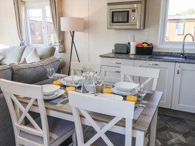 A dining table set with dishes and glasses next to a kitchen with cabinets and a microwave at Honeysuckle Lodge in Runswick Bay near Staithes