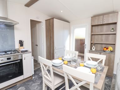 A kitchen and dining area with a table set for four with plates glasses and orange juice at Honeysuckle Lodge Runswick Bay near Staithes
