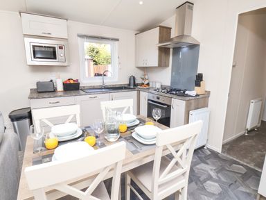 A kitchen with a dining table set for four with plates and glasses at Honeysuckle Lodge in Runswick Bay near Staithes