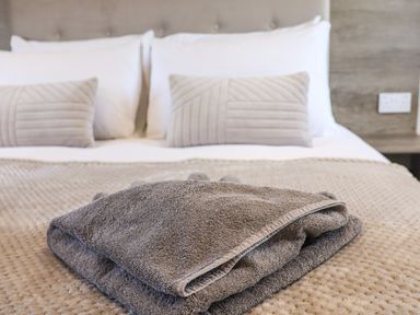 A bed with folded towels on a beige blanket and pillows in a bedroom at Honeysuckle Lodge in Runswick Bay near Staithes