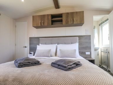 A bedroom with a bed towels on the bed overhead cabinets and a view into a bathroom at Honeysuckle Lodge in Runswick Bay near Staithes