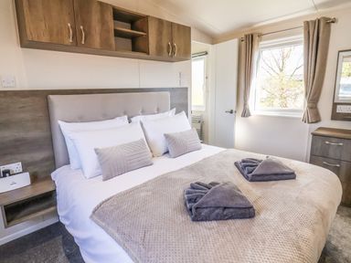 A bedroom with a double bed folded towels on the bed and wooden cabinets above at Honeysuckle Lodge in Runswick Bay near Staithes