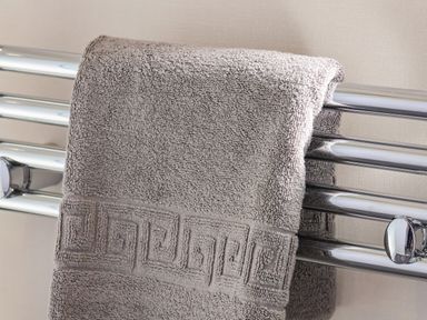 A gray towel hanging on a chrome heated towel rail on a beige wall