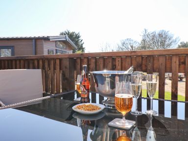 An outdoor patio table with glasses of drinks a bowl of snacks and a bottle in an ice bucket on the table at Honeysuckle Lodge in Runswick Bay near Staithes