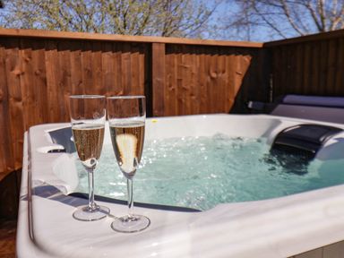 A hot tub with two glasses of sparkling wine on the ledge and a wooden fence in the background at Honeysuckle Lodge in Runswick Bay near Staithes