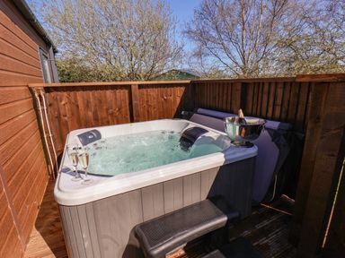 An outdoor hot tub with two glasses of champagne and a bucket with a bottle on a wooden deck at Honeysuckle Lodge in Runswick Bay near Staithes