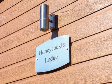 A metal sign with Honeysuckle Lodge text mounted on a wooden exterior wall below a modern metal light fixture at Honeysuckle Lodge in Runswick Bay near Staithes