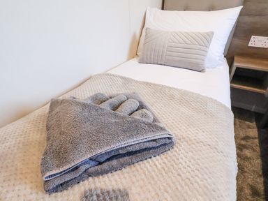 A single bed with a folded grey towel and gray gloves on a beige blanket at Honeysuckle Lodge in Runswick Bay near Staithes