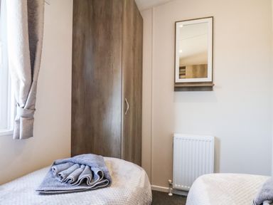 A bedroom with two beds folded towels on one bed a wooden wardrobe a wall mirror and a radiator at Honeysuckle Lodge in Runswick Bay near Staithes