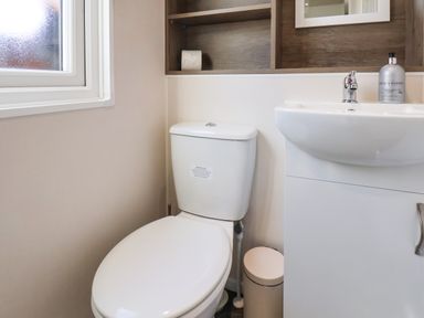 A bathroom with a white toilet sink cabinet window and a small trash can at Honeysuckle Lodge in Runswick Bay near Staithes