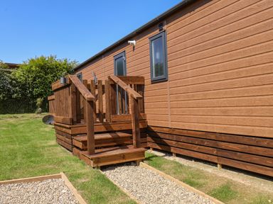 An exterior view of a wooden cabin with small steps and a gravel path outside at Honeysuckle Lodge in Runswick Bay near Staithes