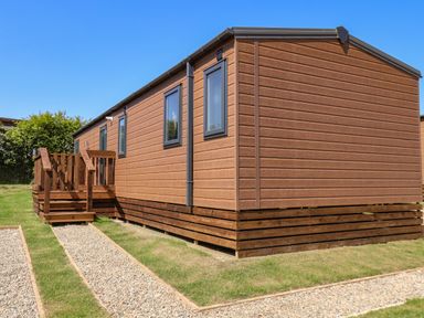 A brown wooden mobile home with small deck steps on a grassy plot at Honeysuckle Lodge in Runswick Bay near Staithes