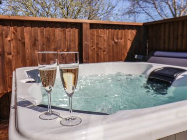 Two glasses of champagne on the edge of a bubbling hot tub with wooden fencing and trees in the background at Lilac Lodge in Runswick Bay near Staithes