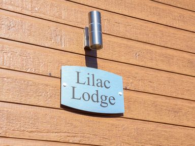A blue sign with Lilac Lodge on a wooden wall under a metal light at Lilac Lodge in Runswick Bay near Staithes