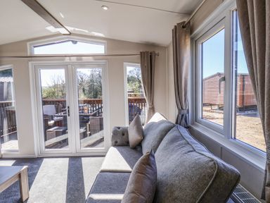 A living room with a gray sofa and large windows showing a deck with outdoor furniture at Lilac Lodge in Runswick Bay near Staithes