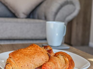 A plate with pastries and a white mug on a wooden table in front of a grey sofa at Lilac Lodge in Runswick Bay near Staithes
