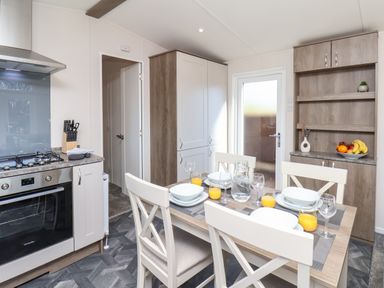 A kitchen and dining area with a stove, knife block, dining table set with plates and glasses, cabinets, and a door at Lilac Lodge Runswick Bay near Staithes