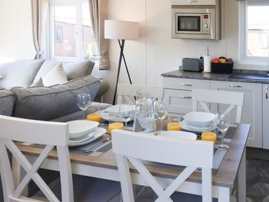 A dining table with plates glasses and orange juice near a sofa and kitchen with microwave in a living area at Lilac Lodge Runswick Bay near Staithes