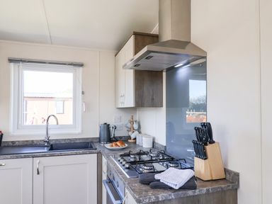 A kitchen with a sink, gas stove, knife block, kettle, and countertop at Lilac Lodge in Runswick Bay near Staithes