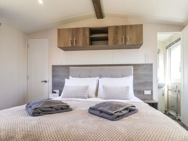 A bedroom with a double bed folded towels two pillows and wooden cabinets at Lilac Lodge in Runswick Bay near Staithes