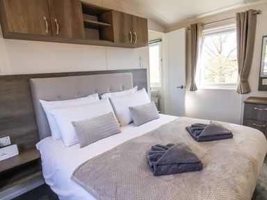 A bedroom with a bed folded towels on a beige blanket and wooden cabinets above the headboard at Lilac Lodge in Runswick Bay near Staithes