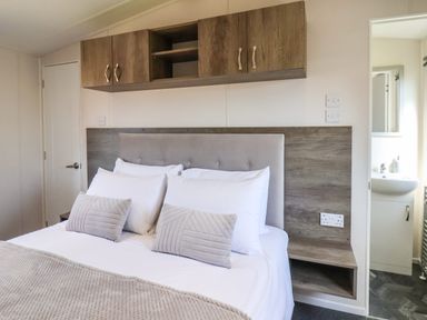 A bedroom with a bed with pillows and a blanket wooden cabinets above the bed and a small sink area visible through an open door at Lilac Lodge in Runswick Bay near Staithes