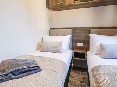 A bedroom with two single beds with pillows blankets and a bedside table in between at Lilac Lodge in Runswick Bay near Staithes
