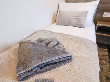 A single bed with white sheets a beige blanket and folded gray towels on top at Lilac Lodge in Runswick Bay near Staithes