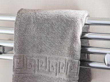 A gray towel hanging on a chrome heated towel rail in a bathroom
