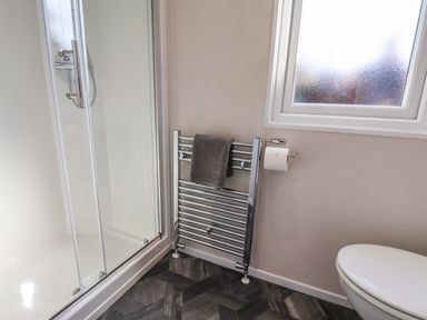 A bathroom with a shower enclosure a towel rail with a towel a toilet and a frosted window at Lilac Lodge in Runswick Bay near Staithes