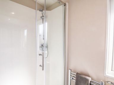 A bathroom shower with glass door and a towel hanging on a radiator at Lilac Lodge in Runswick Bay near Staithes