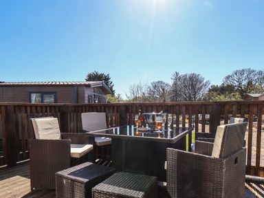 An outdoor seating area with a glass table and wicker chairs on a wooden deck at Lilac Lodge in Runswick Bay near Staithes