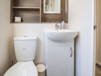 A bathroom with a toilet sink cabinet and wall shelves at Lilac Lodge in Runswick Bay near Staithes