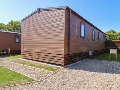 An exterior view of a brown wooden lodge with gravel paths and grassy areas at Lilac Lodge in Runswick Bay near Staithes