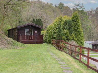A wooden cabin with a small porch surrounded by grass trees and a wooden fence at Canadian Cabin 37 in Keswick