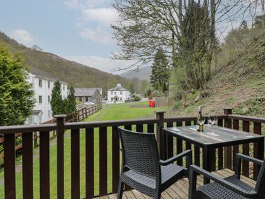 A balcony with a table and two chairs overlooking greenery and houses at Canadian Cabin 37 in Keswick