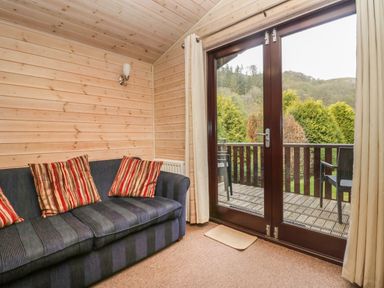 A cabin room with a striped sofa and cushions next to glass doors leading to a balcony with chairs at Canadian Cabin 37 in Keswick