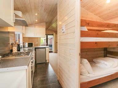 A kitchen with stove, microwave, fridge, and a bunk bed in an adjacent room at Canadian Cabin 37 in Keswick