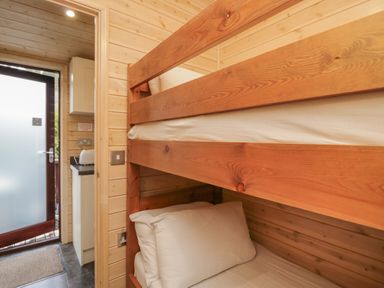 A bedroom with wooden bunk beds and a door leading to a kitchenette at Canadian Cabin 37 in Keswick