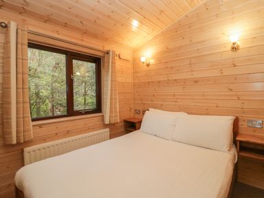A bedroom with a double bed white bedding wooden walls two wall lamps a window with beige curtains and a radiator below Canadian Cabin 37 Keswick