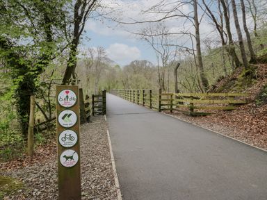 A paved forest trail with wooden railings and multiple signs indicating to keep left, slow down cyclists, and use short dog leads at Canadian Cabin 37 in Keswick
