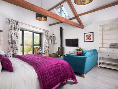 A bedroom with a bed purple blanket teal sofa yellow chair wood stove and window at Shepherds View Dufton near Appleby-in-Westmorland