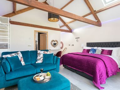 A bedroom with a purple bed, teal sofa, wooden beams on ceiling, and a tray with snacks at Shepherds View in Dufton near Appleby-in-Westmorland