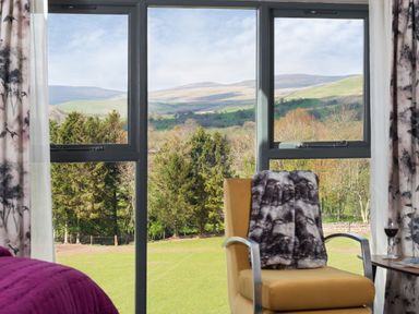 A chair with a blanket by a window overlooking trees and hills at Shepherds View in Dufton near Appleby in Westmorland