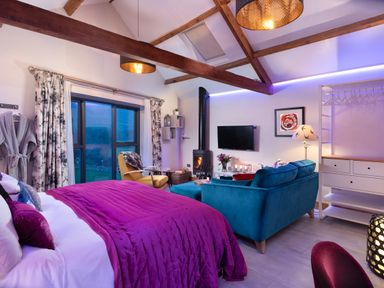 A bedroom with a purple bedspread a teal sofa a yellow armchair a wood stove and a mounted television at Shepherds View Dufton near Appleby-in-Westmorland