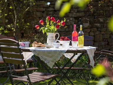 An outdoor garden table with a white lace tablecloth holding flowers bread, strawberries, and drinks at Shepherds View in Dufton, near Appleby-in-Westmorland