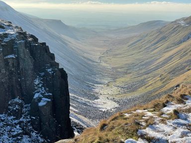 A mountain valley with a rocky cliff and patches of snow and grass at Shepherds View in Dufton near Appleby-in-Westmorland